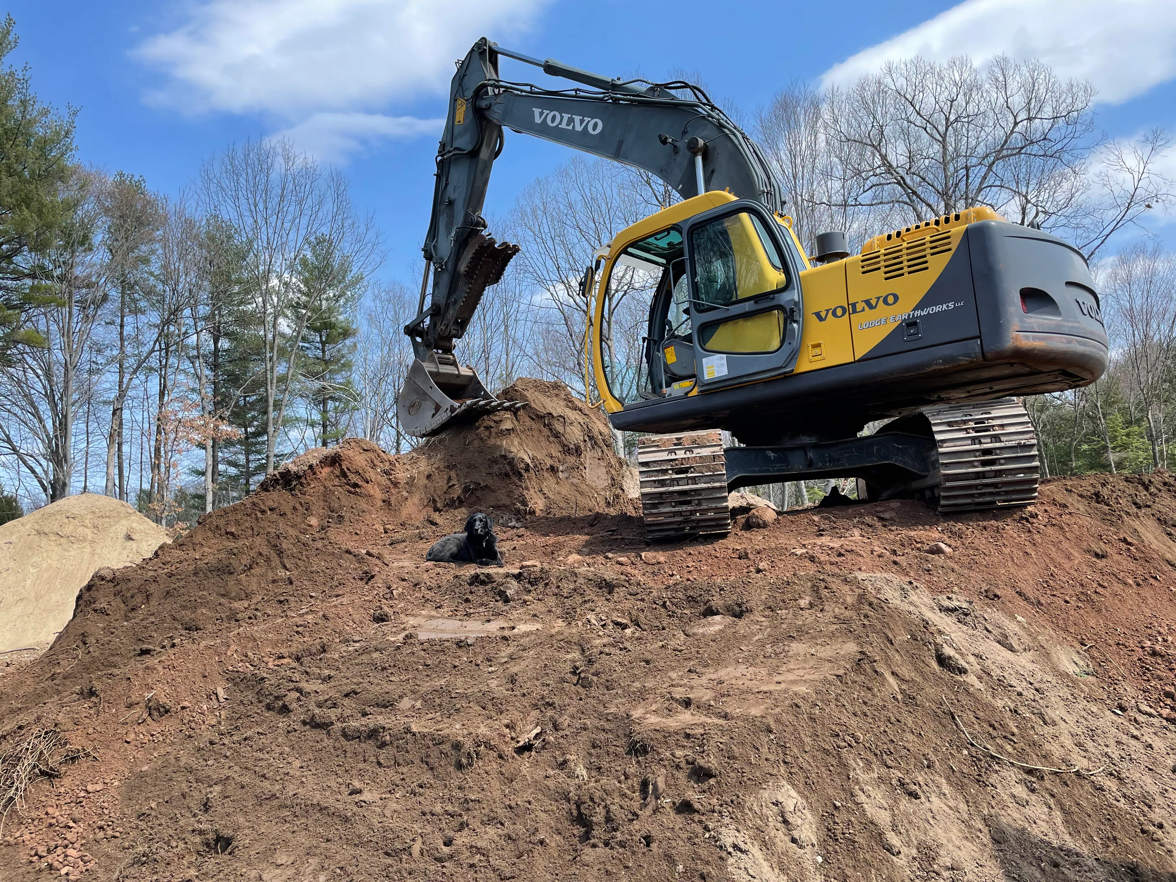 A Volvo with a Lodge Earthworks decal on a mound of dirt with a black labradoor dog laying down in the corner.